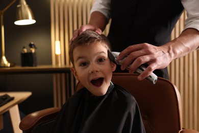 Photo of Professional barber working with little boy in barbershop, closeup