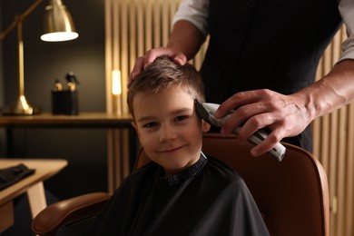 Photo of Professional barber working with little boy in barbershop, closeup