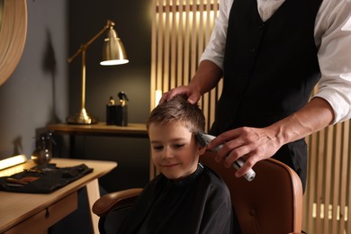 Photo of Professional barber working with little boy in barbershop, closeup