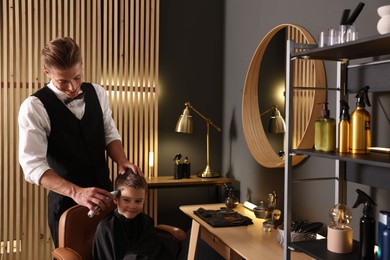 Photo of Professional barber working with little boy in barbershop