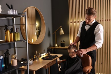 Photo of Professional barber working with little boy in barbershop