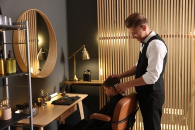 Photo of Professional barber working with little boy in barbershop