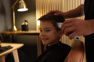 Photo of Professional barber working with little boy in barbershop, closeup