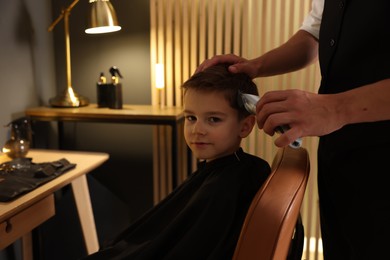Photo of Professional barber working with little boy in barbershop, closeup