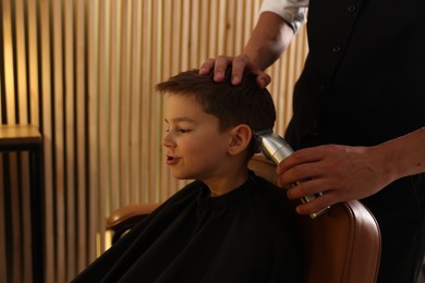 Photo of Professional barber working with little boy in barbershop, closeup