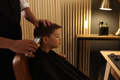 Photo of Professional barber working with little boy in barbershop, closeup