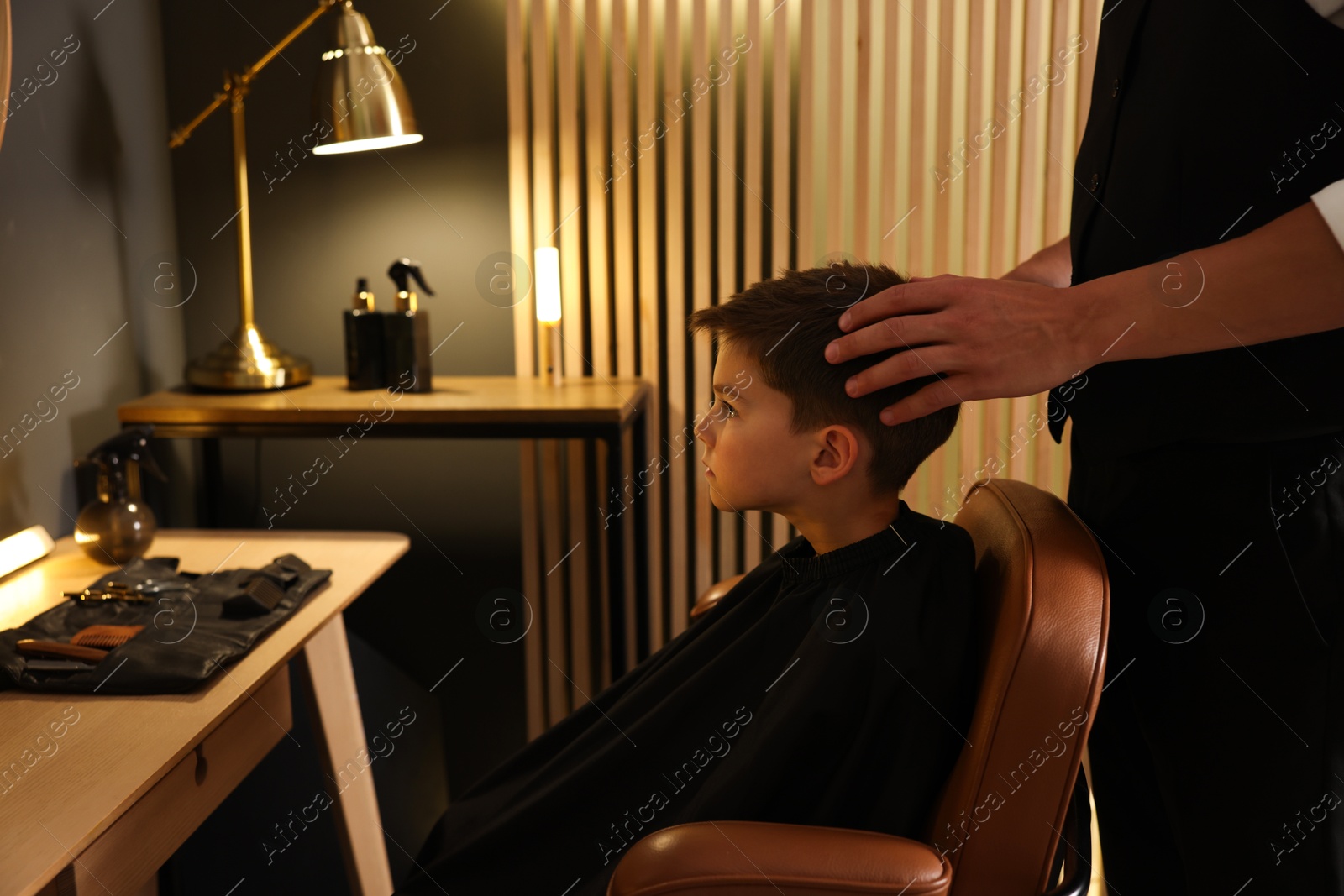Photo of Professional barber working with little boy in barbershop, closeup