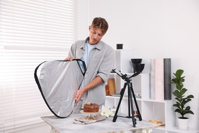 Photo of Man using reflector to take picture of chocolate cake in studio. Professional food photography