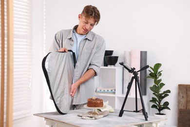 Photo of Man using reflector to take picture of chocolate cake in studio. Professional food photography