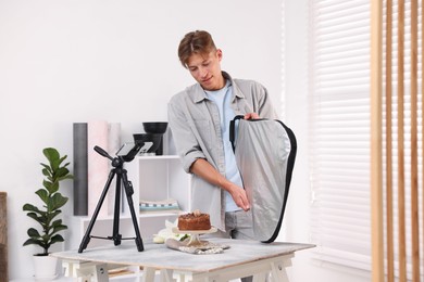 Photo of Man using reflector to take picture of chocolate cake in studio. Professional food photography