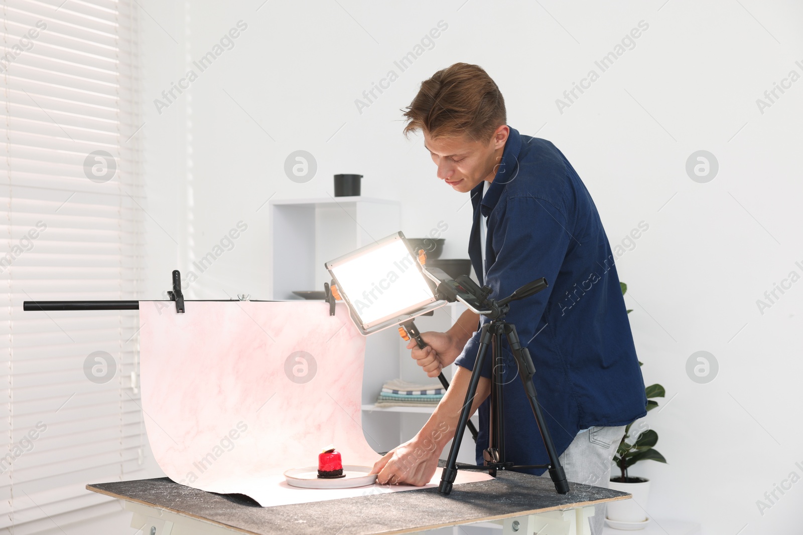 Photo of Man using lighting equipment to take picture of tasty dessert in studio. Professional food photography