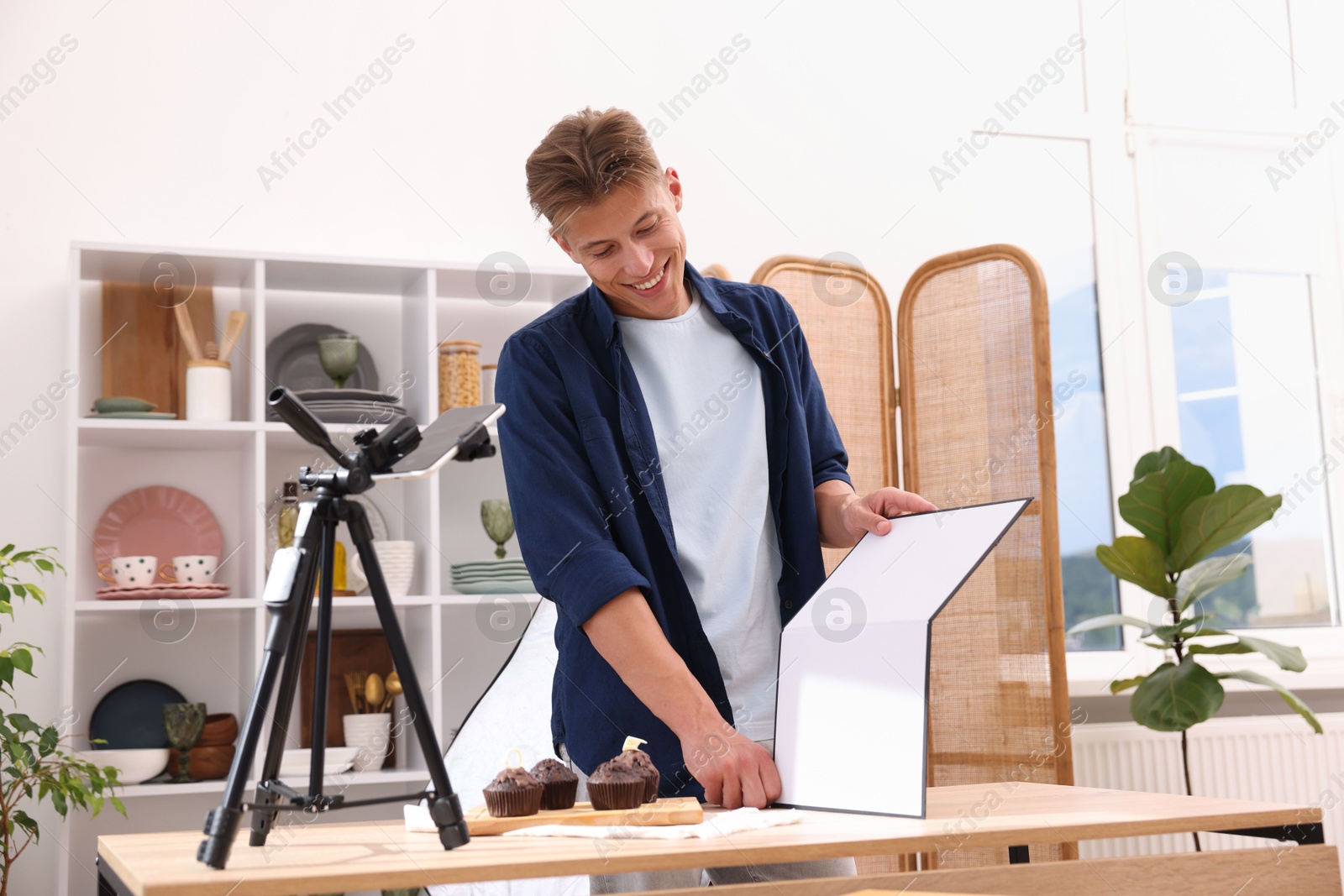 Photo of Man using reflector to take picture of chocolate muffins in studio. Professional food photography
