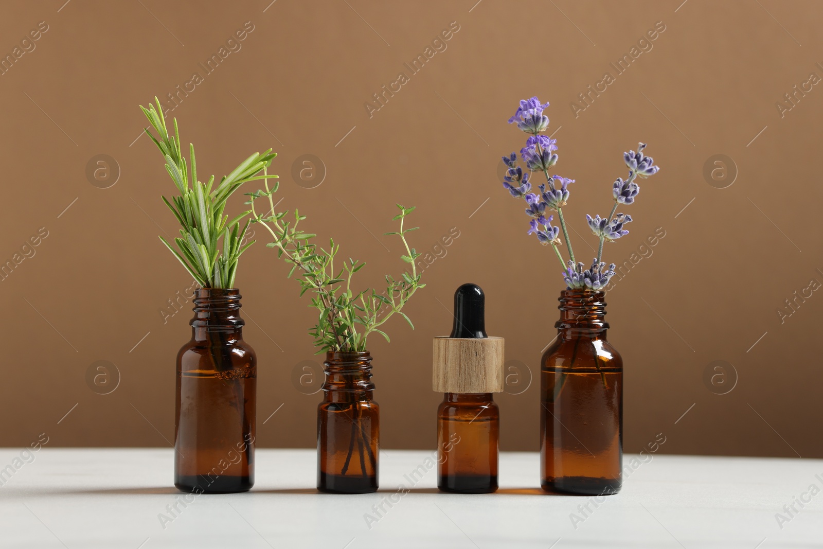 Photo of Different herbs in glass bottles and essential oil on white table against brown background