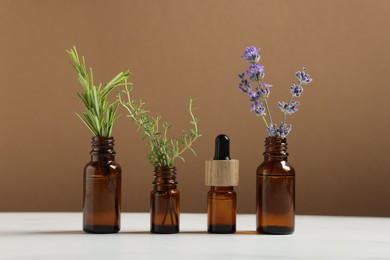 Photo of Different herbs in glass bottles and essential oil on white table against brown background