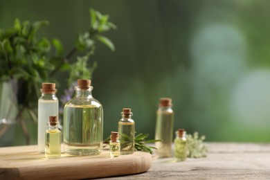 Photo of Bottles of essential oils and different herbs on wooden table outdoors, closeup. Space for text