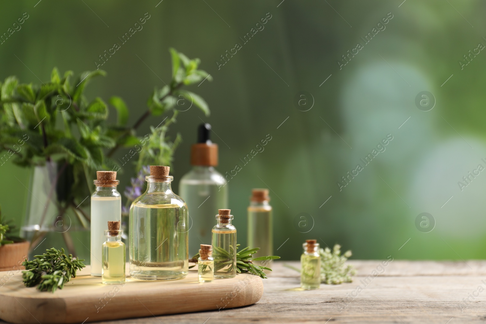 Photo of Bottles of essential oils and different herbs on wooden table outdoors, closeup. Space for text