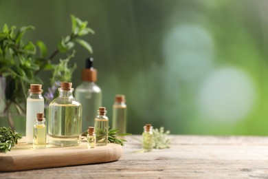 Photo of Bottles of essential oils and different herbs on wooden table outdoors, closeup. Space for text