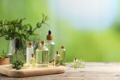 Photo of Bottles of essential oils and different herbs on wooden table outdoors, space for text
