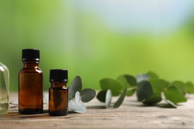 Photo of Bottles of essential oils and eucalyptus branch on wooden table outdoors, closeup