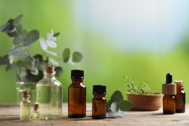 Photo of Bottles of essential oils, eucalyptus branches and thyme on wooden table outdoors, closeup