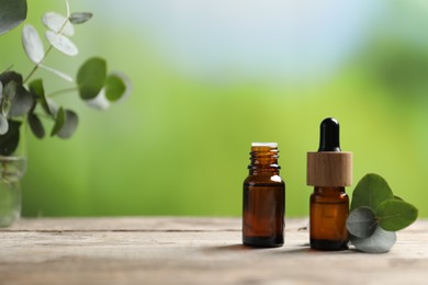 Photo of Bottles of essential oils and eucalyptus branches on wooden table outdoors, closeup. Space for text