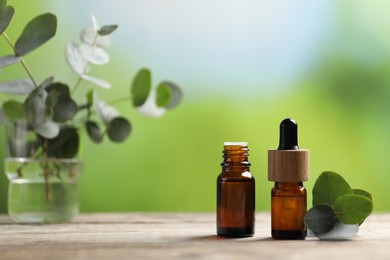 Photo of Bottles of essential oils and eucalyptus branches on wooden table outdoors, closeup. Space for text
