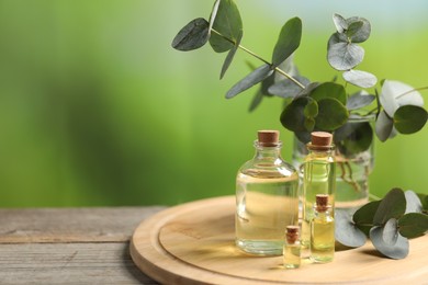 Photo of Bottles of essential oils and eucalyptus branches on wooden table outdoors, closeup. Space for text