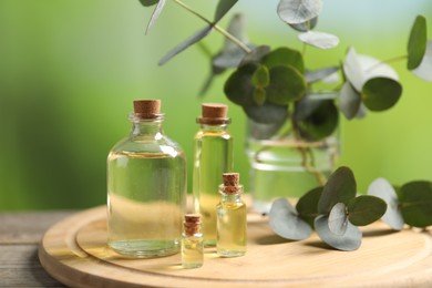 Photo of Bottles of essential oils and eucalyptus branches on wooden table outdoors, closeup