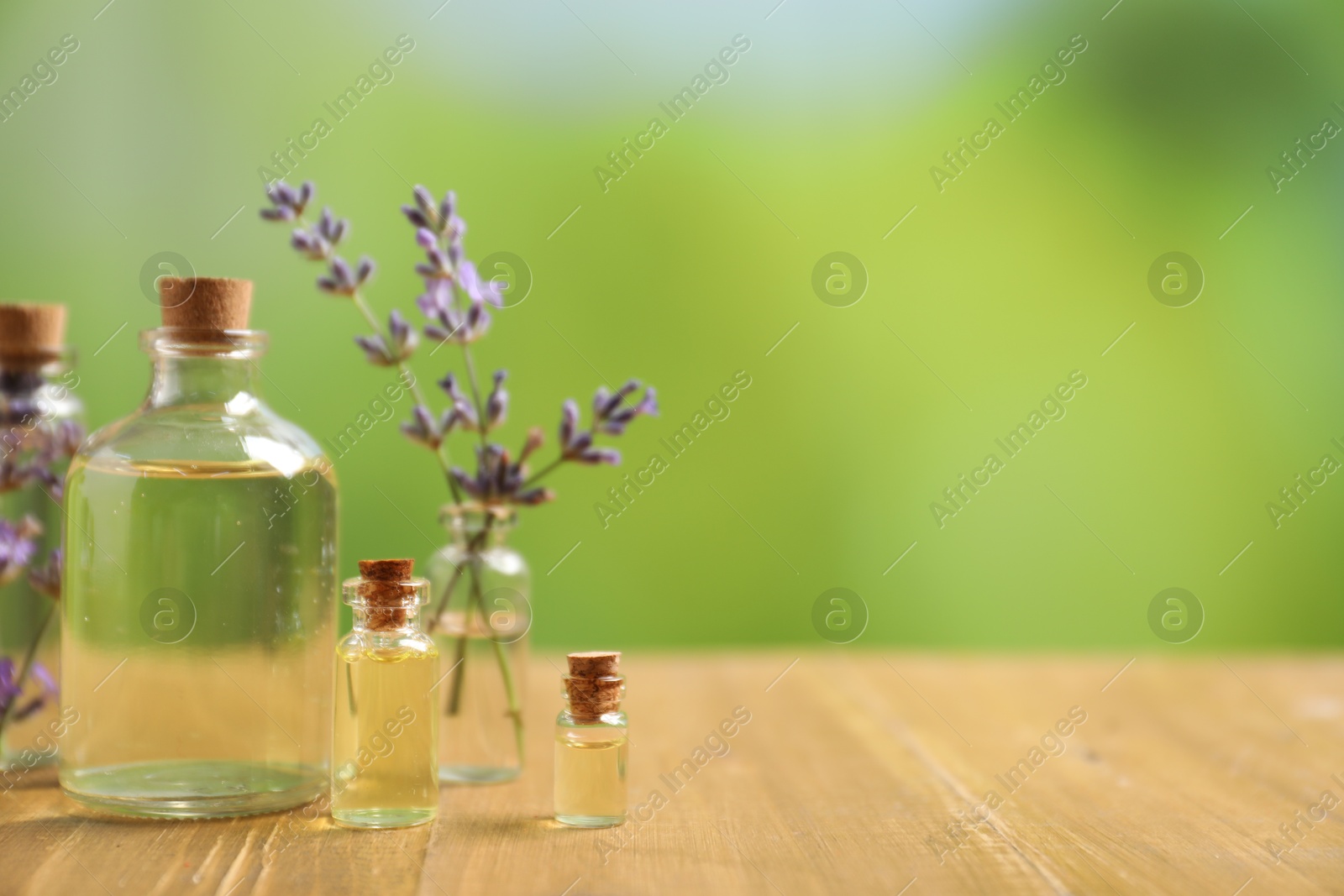Photo of Bottles of essential oils and lavender flowers on wooden table outdoors, closeup. Space for text