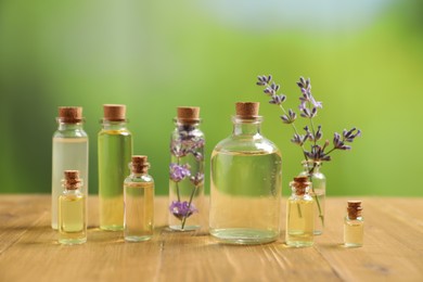 Photo of Bottles of essential oils and lavender flowers on wooden table outdoors