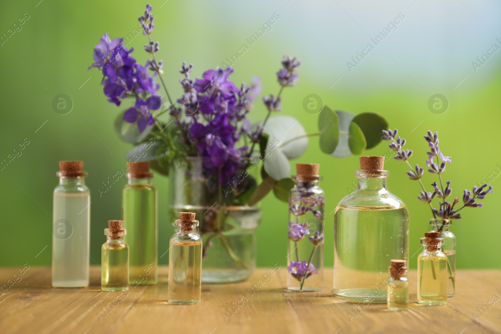 Photo of Bottles of essential oils and different plants on wooden table outdoors, closeup
