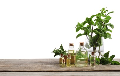 Photo of Bottles of essential oils, mint and thyme on wooden table against white background
