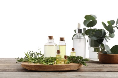 Photo of Bottles of essential oils, thyme, eucalyptus leaves and rosemary on wooden table against background