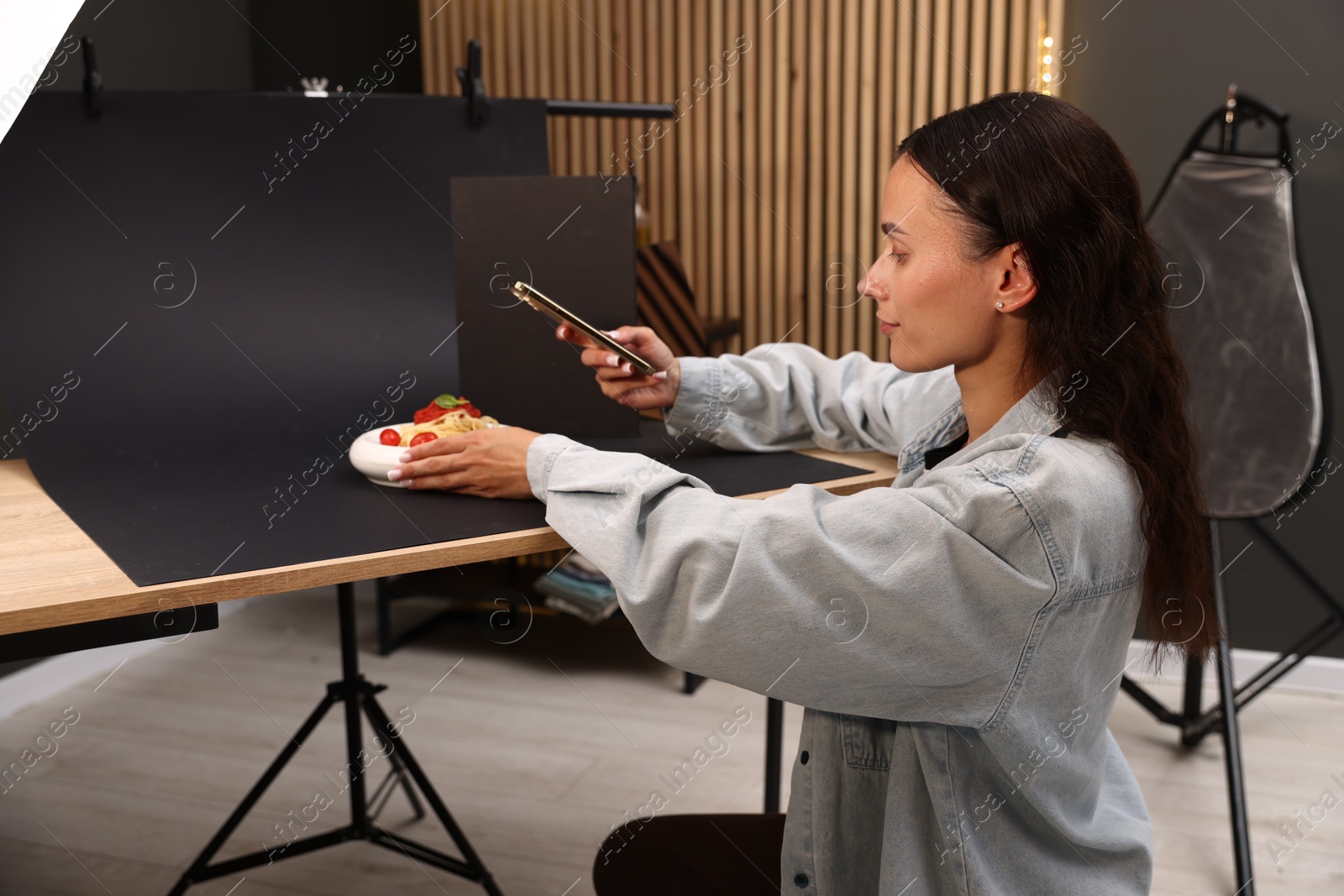 Photo of Woman taking picture of tasty pasta with smartphone in studio. Professional food photography