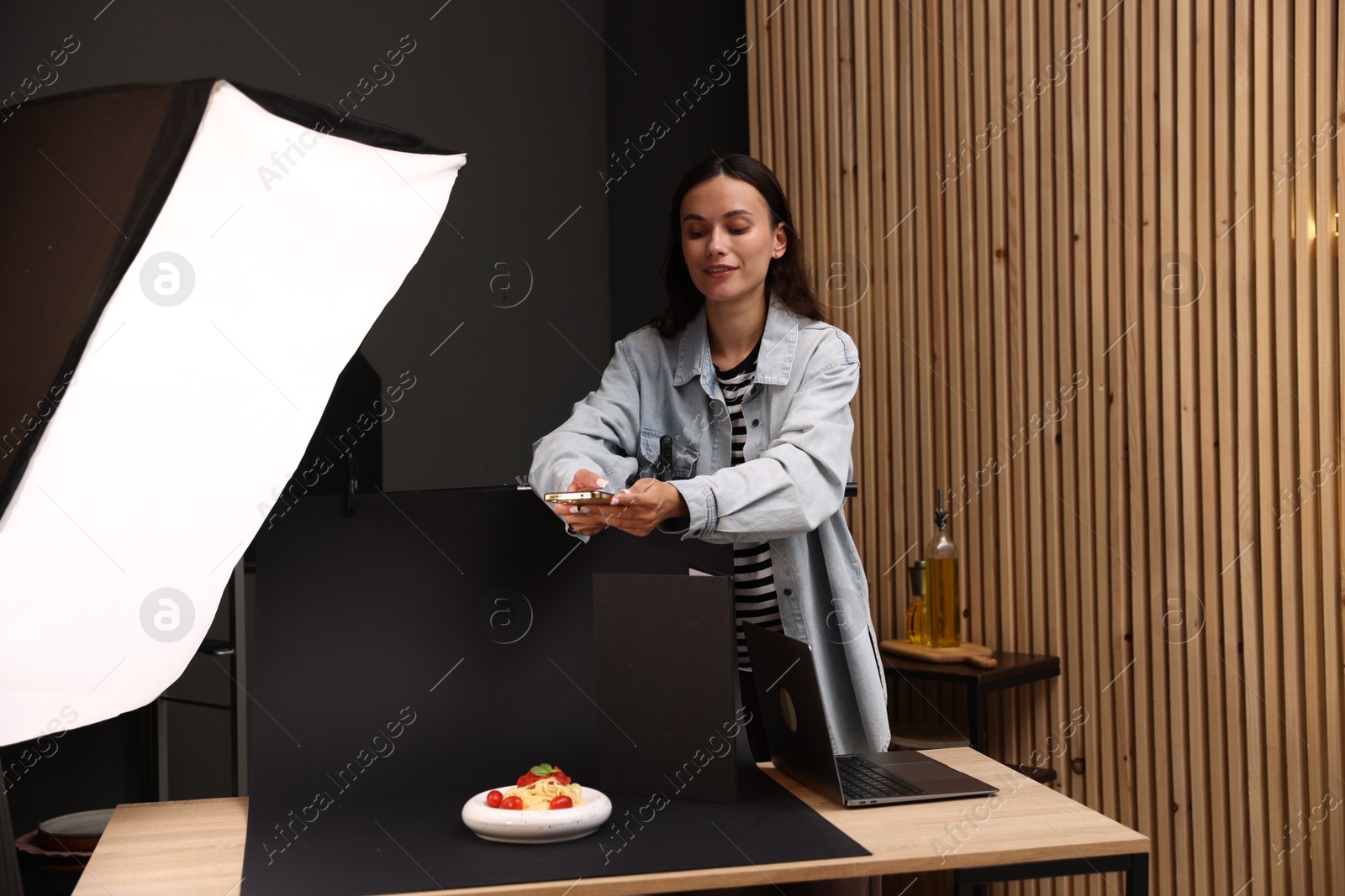 Photo of Woman taking picture of tasty pasta with smartphone in studio. Professional food photography