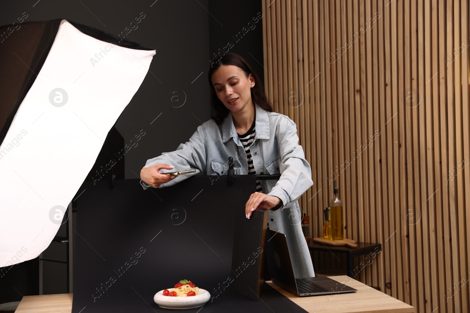 Photo of Woman taking picture of tasty pasta with smartphone in studio. Professional food photography