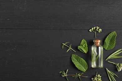 Photo of Essential oil and different plants on black wooden background, flat lay. Space for text