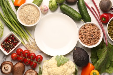 Photo of Healthy vegetarian food. Empty plate surrounded by different products on white marble table, flat lay