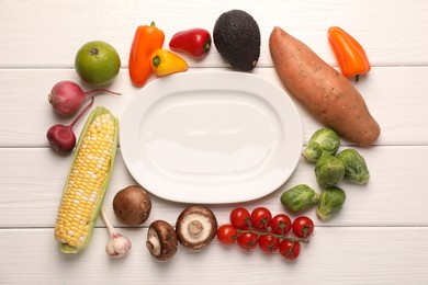 Photo of Healthy vegetarian food. Empty plate surrounded by different products on white wooden table, flat lay