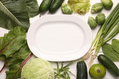 Photo of Healthy vegetarian food. Empty plate surrounded by different products on white wooden table, flat lay
