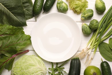 Photo of Healthy vegetarian food. Empty plate surrounded by different products on white wooden table, flat lay