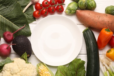 Photo of Healthy vegetarian food. Empty plate surrounded by different products on white wooden table, flat lay