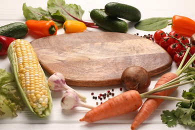 Photo of Healthy vegetarian food. Empty board surrounded by different products and peppercorns on white wooden table, closeup