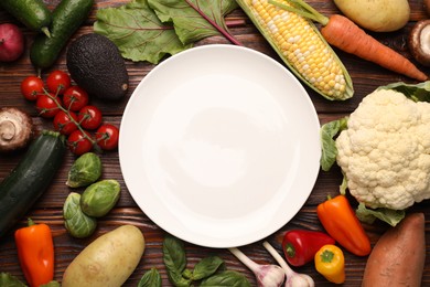 Photo of Healthy vegetarian food. Empty plate surrounded by different products on wooden table, flat lay