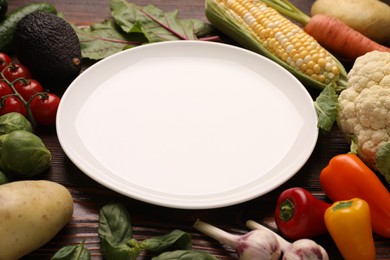 Photo of Healthy vegetarian food. Empty plate surrounded by different products on wooden table, closeup