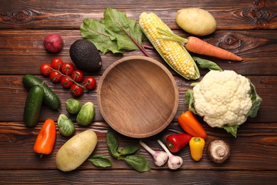 Photo of Healthy vegetarian food. Empty plate surrounded by different products on wooden table, flat lay