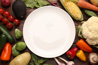 Photo of Healthy vegetarian food. Empty plate surrounded by different products on wooden table, flat lay