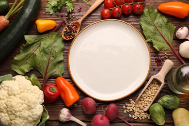 Photo of Healthy vegetarian food. Empty plate surrounded by different products on wooden table, flat lay