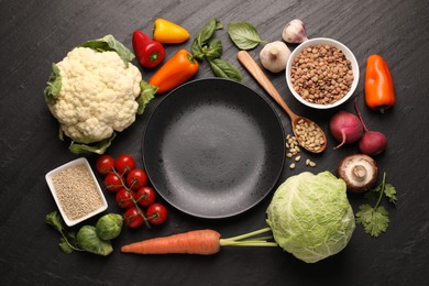 Photo of Healthy vegetarian food. Empty plate surrounded by different products on dark textured table, flat lay