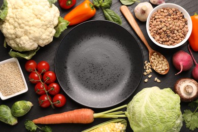 Photo of Healthy vegetarian food. Empty plate surrounded by different products on dark textured table, flat lay